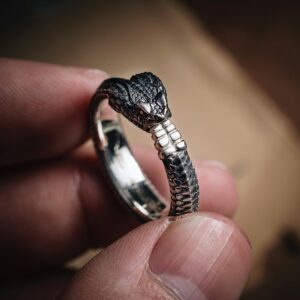 Detailed close-up of a handmade snake ring held by human fingers, showcasing intricate craftsmanship.